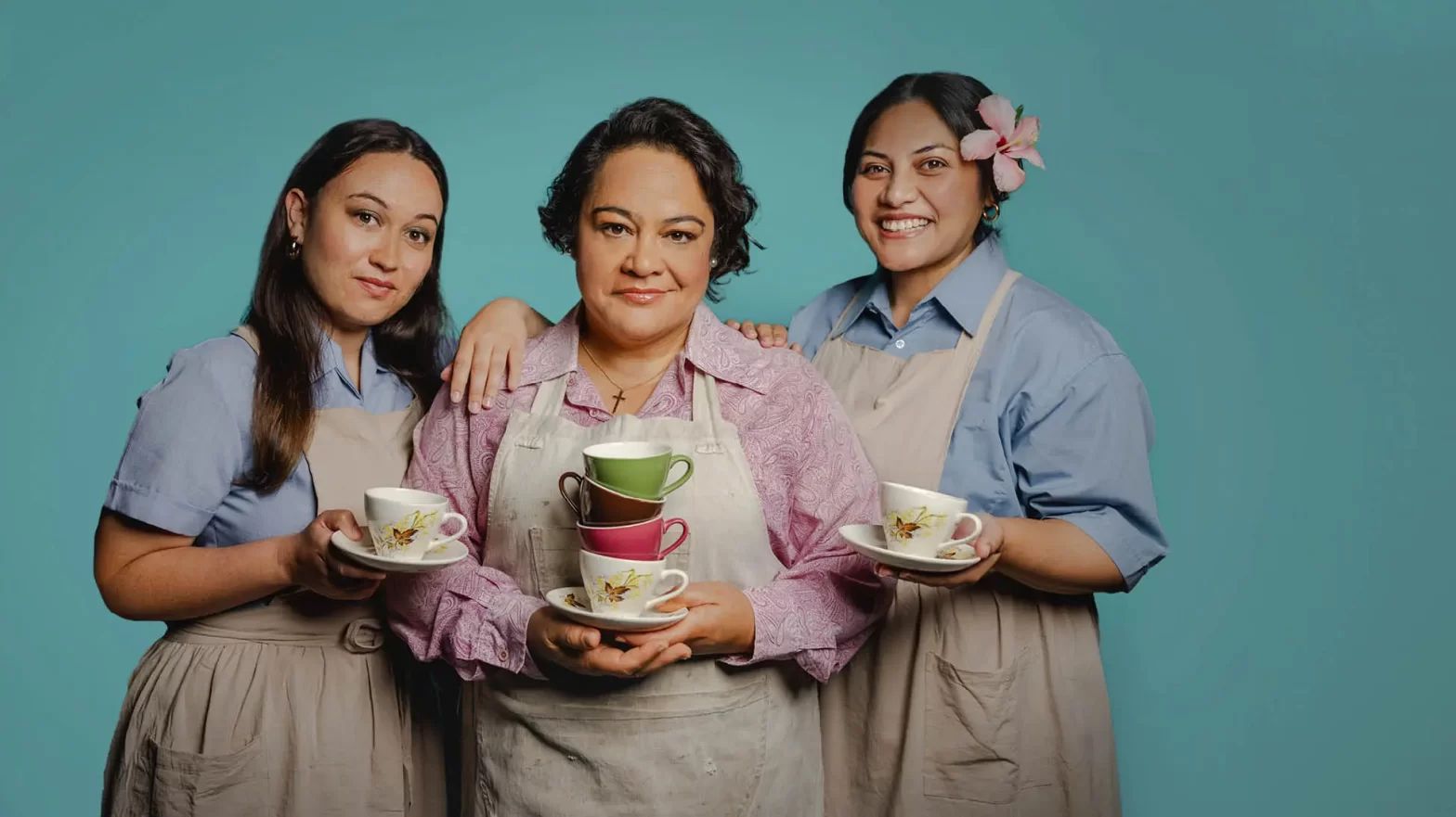 Three women stand together, dressed in work uniforms holding teacups